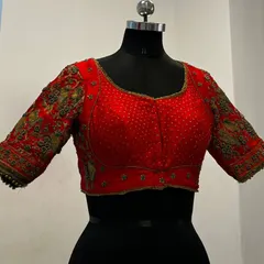 A still image of a vibrant red blouse, showcasing the pearl-like embellishments on the body and the heavy, multi-colored threadwork on the sleeves. This type of detailed craftsmanship is perfect for our rental platform.