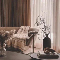 A cozy corner concept, perfect for reading. The design uses layers of texture, from the soft throw blanket to the dried botanicals and dark, sculptural vase, creating a warm and inviting nook.