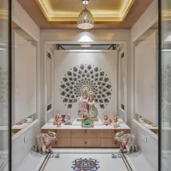 This elegant pooja room combines classic and contemporary elements, featuring a detailed peacock feather inlay on a marble wall. The space is symmetrically designed with silver elephant statues, a modern pendant light, and ample storage in the base cabinet.