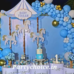 A full view of a carousel-themed party at night by the pool. The setup is beautifully lit, with the cake and desserts displayed on themed pedestals in front of the main backdrop.