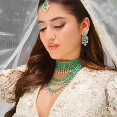 An ethereal bridal look in ivory, accented with emeralds. The makeup is fresh and radiant, with a focus on a dewy complexion and soft pink tones to complement the modern bride's aesthetic.