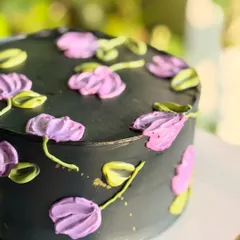 A detailed shot of the black floral cake, focusing on the texture and color variation in the palette knife flowers and the subtle gold splatter.
