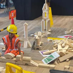 I believe in the power of play, and our dedicated kids' zones are designed for exactly that. Here, a young engineer is completely absorbed in building with giant wooden blocks, an example of the open-ended, creative fun I arrange to keep your children happily engaged.