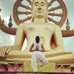 In a moment of reverence during a trip to Thailand, practicing a balancing pose before a great Buddha statue. This image reflects the truth that conquering oneself is the greatest victory.