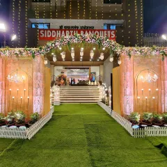 This pastel-themed entrance was created for a reception at Siddharth Banquets. The design features a floral arch in soft pinks and whites, elegant wall panels with chandelier motifs, and warm lighting for a romantic feel.