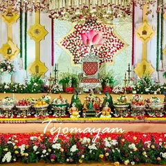 A vibrant half-saree ceremony setup with a backdrop of colorful flowers and a full, beautifully arranged display of traditional plates.