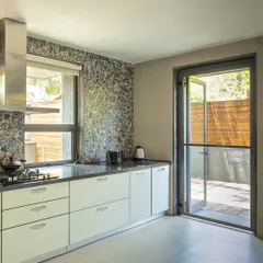 This kitchen design embraces natural light with a large window over the counter. The door provides direct access to an outdoor space, blurring the line between inside and out and making the kitchen feel airy and connected to nature.