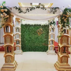 This mantap, designed for a baby shower, uses ornate pillars and a green foliage backdrop. A custom monogram with the couple's initials adds a personal touch to the traditional structure.