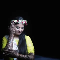 A close-up portrait focusing on the intricate Mehendi design on the bride's hands and arms. Her floral tiara and serene expression add to the beauty of this pre-wedding ritual.