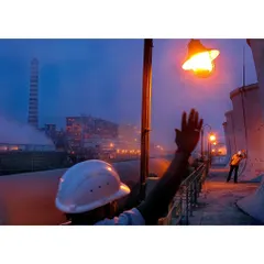 A shot capturing workers at a power plant during dusk. The composition uses the warm glow of an industrial lamp to highlight the human presence and scale of the environment.