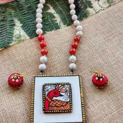This Gond art style deer painting on a square terracotta pendant is a unique fusion of tribal art and modern jewelry design. The set includes matching jhumkas and is available in a red and white color scheme.