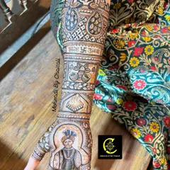A side view of a groom's portrait on the bride's arm. The design includes peacocks and auspicious symbols, all drawn with fine lines and careful shading to bring the artwork to life.