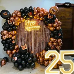 Here is another take on a 25th-anniversary celebration, using a modern color scheme. The setup includes a full balloon ring of black and rose gold chrome balloons, a rose gold fringe curtain, a "Happy Anniversary" neon sign, and illuminated "25" numbers.