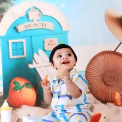 A joyful baby boy enjoys a snack in our sunny beach-themed set, complete with a beach hut, sand, and fruity props.