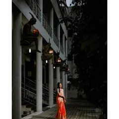 An artistic and moody portrait of the bride at her reception, her vibrant saree a beautiful pop of color against the dark, architectural background.