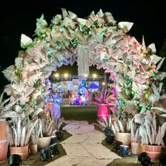 A grand entrance arch designed with a bohemian theme. The structure is covered in dried pampas grass and palm leaves, with a central macrame hanging, creating a dramatic and stylish welcome for a rustic-themed event.