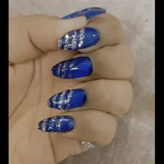 A close-up of a bold and glamorous design. These almond-shaped extensions feature a vibrant royal blue base with striking silver glitter stripes for a look that's sure to turn heads.
