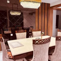 An elegant dining area designed for memorable gatherings. The space is defined by a stunning crystal chandelier, a reflective smoked-glass wall that enhances the sense of space, and luxurious upholstered chairs for ultimate comfort.