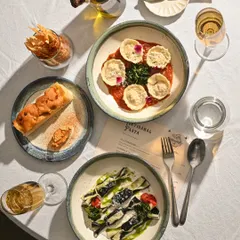 A table set for a feast. Here you see my artisanal pasta dishes, including Carmelle in a rich tomato sauce and a striped Farfalle, ready to be enjoyed with wine and focaccia.