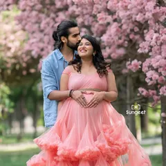 A joyful moment between an expecting couple, surrounded by blooming pink Tabebuia flowers. We know the best seasonal spots in Bangalore for stunning floral backdrops.