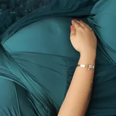 An intimate detail shot focusing on a hand gently resting on the baby bump, showcasing a beautiful bracelet and the rich color of the teal gown.