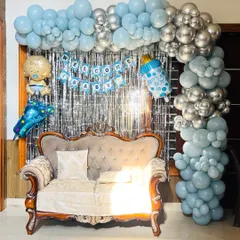 A 'Welcome Baby' setup with a silver tinsel backdrop and an L-shaped balloon arch in shades of blue and silver.