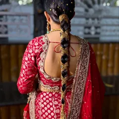 A stunning traditional braid for a North Indian bride, intricately decorated with gold accessories to match her red lehenga.
