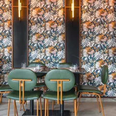 The seating at Burosu features custom-designed green chairs with unique T-shaped backs, set against a bold tropical wallpaper. This combination of bespoke furniture and dynamic patterns contributes to the restaurant's energetic vibe.
