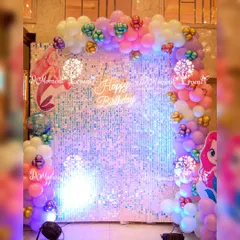 This mermaid-themed photo backdrop uses an iridescent sequin wall to create a shimmering underwater effect. The scene is framed with a vibrant balloon garland and character cutouts, perfect for capturing magical birthday photos.