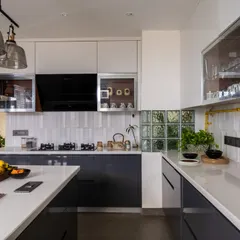 A wider view of the industrial-transitional kitchen, showing the U-shaped layout. The design features a mix of glossy white and grey cabinets, a white subway tile backsplash, and a glass block window for added light.