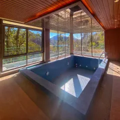 The indoor plunge pool at the Uttarakhand homestay. Surrounded by floor-to-ceiling glass and a skylight, this space allows for a swim with an uninterrupted view of the forest and mountains.