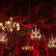 A ceiling full of hanging chandeliers against a backdrop of royal red drapes creates an atmosphere of pure opulence.