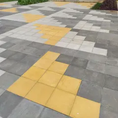 A playful pixelated pattern created with concrete pavers in shades of grey and yellow. This detail adds a touch of color and graphic interest to a large paved area in a residential layout.