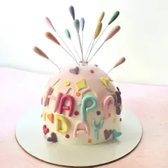 A fun and festive "piñata" style bomb cake. The dome shape is decorated with colorful letters and a firework-like topper, ready for a celebration.