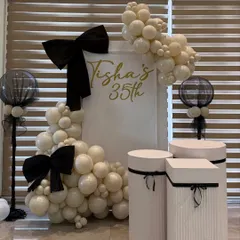 For a chic 35th birthday, we designed a sophisticated black, white, and gold theme. This setup features custom signage, elegant plinths for the cake display, and organic balloon garlands accented with statement bows for a touch of modern glamour.