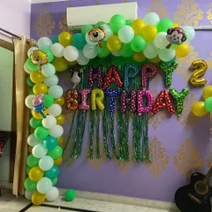 A fun jungle safari theme for a kid's birthday party at home. This setup includes a green and yellow balloon arch with animal character foils and a 'Happy Birthday' backdrop.