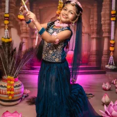 Dressed as Radha, this young girl's graceful pose and joyful smile are captured against our elaborate temple-themed studio backdrop. We pay close attention to every detail, from the traditional attire to the props.