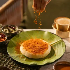 A hand sprinkling podi masala over a soft idli. This action shot highlights the fresh spices and adds a dynamic element to the photo.