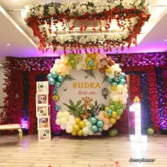 This close-up shows the centerpiece of the 'Rudra turns one' jungle party. The custom circular backdrop is framed by a beautiful organic balloon garland in jungle colors, with adorable animal characters peeking through. The marquee '1' adds a special touch.