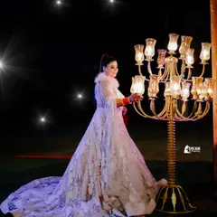 A full-length shot capturing the magnificent trail of Deepakshi's gown as she poses by a candelabra under the stars.