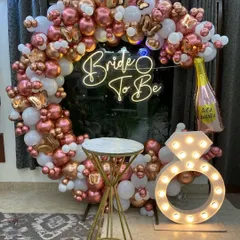 We design stylish photo booths for pre-wedding functions. This 'Bride to Be' setup includes a circular balloon frame in rose gold and white, a custom neon sign, and a light-up marquee ring prop for the perfect pictures.