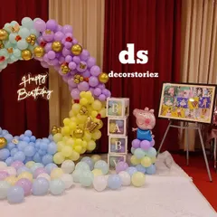 This Peppa Pig first birthday setup in a banquet hall includes a large balloon ring, marquee number, character props, and personalized 'BABY' blocks for a complete photo corner.
