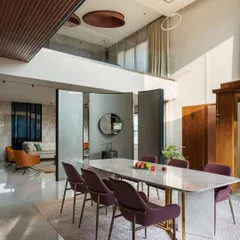 A double-height dining room in the Timber Edge project, overlooked by a glass-railed bridge. The design uses pivoting partitions to create a flexible boundary with the adjacent living area.