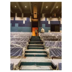 This is the auditorium of the memorial complex during its final stages of construction. The pixelated acoustic wall paneling in shades of blue adds visual interest and functional sound dampening to what is designed as a hub for community events.