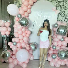 The birthday girl enjoying a drink in front of her custom party decor. This full view shows the scale of the pink and silver balloon arch, creating a glamorous and festive atmosphere perfect for a house party.