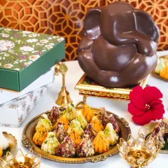 A festive spread for Ganesh Chaturthi, featuring a chocolate Ganesha idol and a platter of assorted modaks. The traditional brass diyas and flowers create a divine and celebratory atmosphere.