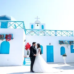 A classic pre-wedding portrait that feels like a fairytale. The couple, dressed in formal black and white, stands against the vibrant blue and white architecture, creating a timeless and romantic photograph.