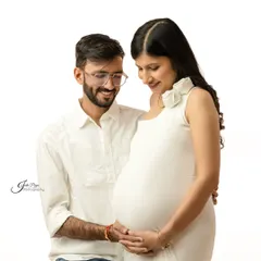 A classic couple's pose against a pure white background. They both look down at the baby bump, sharing a quiet moment of anticipation for their little one's arrival.