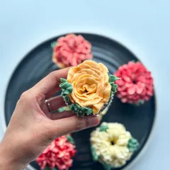A beautiful yellow-orange buttercream rose cupcake with green leaves.