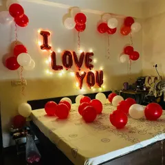 A simple and sweet "I Love You" room decoration. The setup includes red and white balloons on the bed and ceiling, with the message spelled out in foil balloons and backlit by fairy lights.